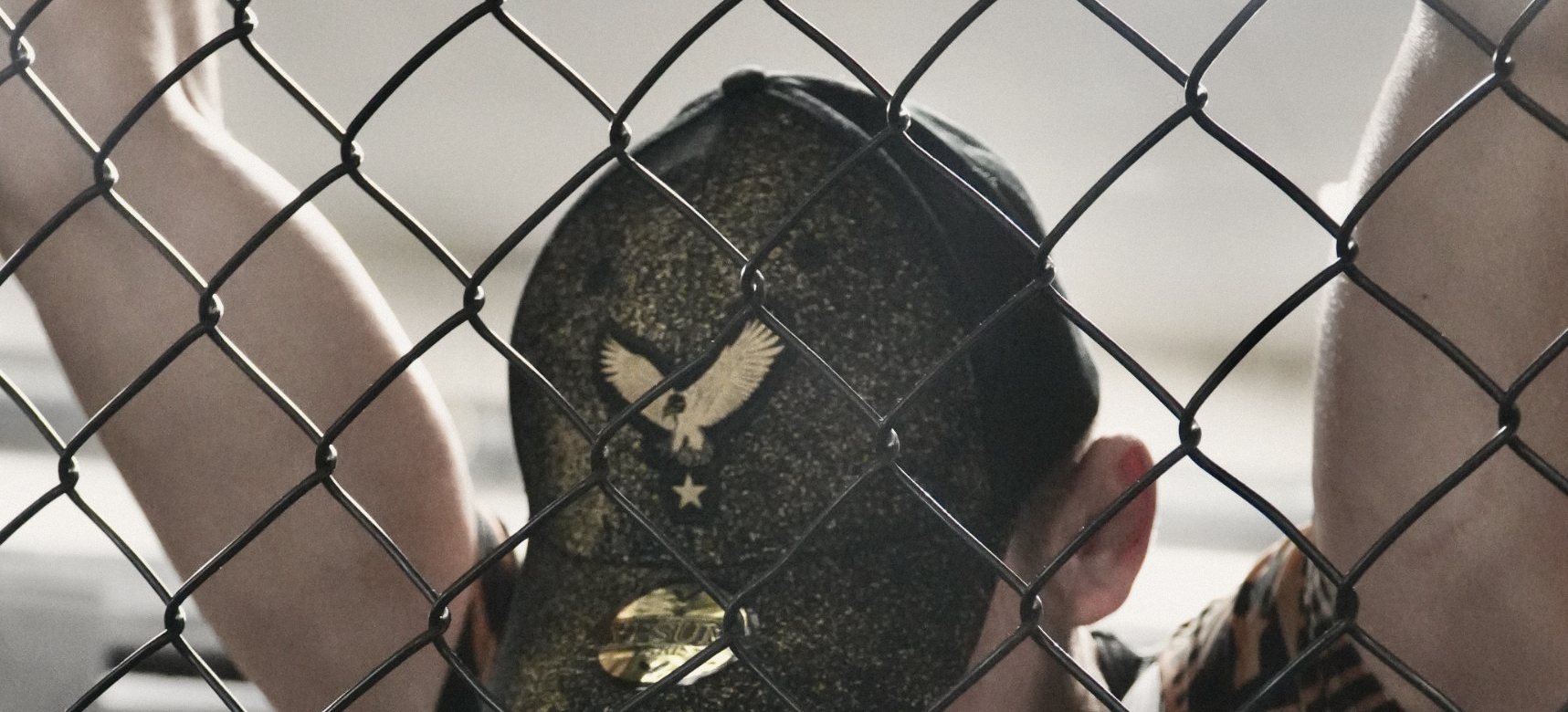 Un combattant agrippé au grillage, le visage caché par la casquette YPSUM